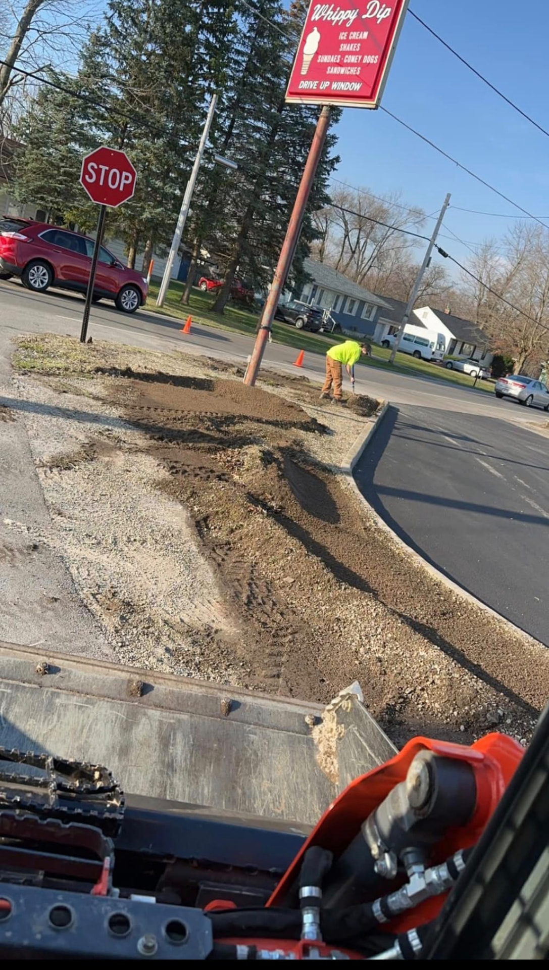 Dirt work and grading along a new asphalt lot with crew member raking